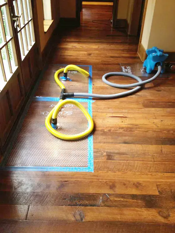 Hardwood floor drying mats taped down over a wet plank floor