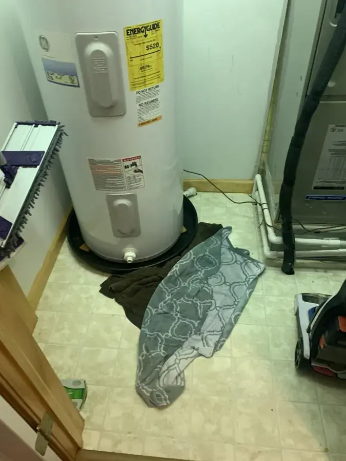 Water heater tank with towels soaking up a leak on a utility room floor
